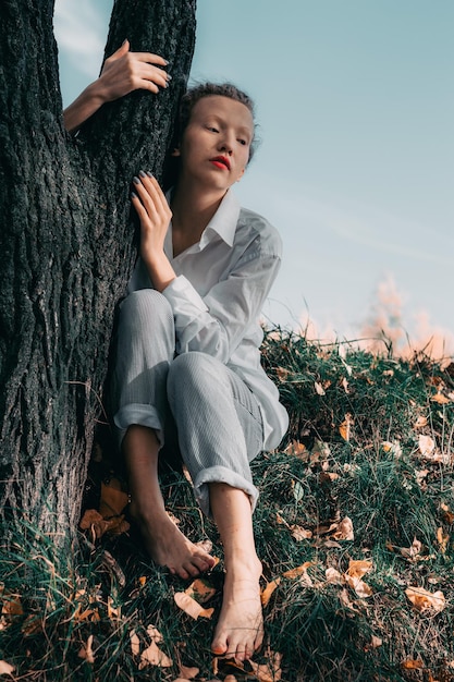 Foto donna seduta sull'erba vicino al tronco dell'albero durante l'autunno