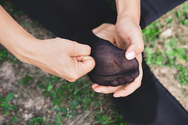 Woman sitting on grass and massages the foot in sock close-up. Pain or cramping in the foot.