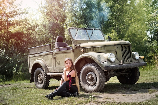 Foto donna seduta per terra vicino a un'auto militare