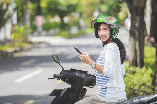 Woman sitting on her motorbike and using mobile phone