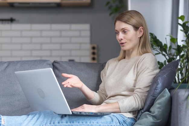 Woman sitting at home on the couch in the kitchen using a laptop for a video call talking to friends remotely