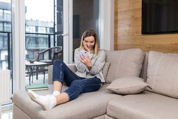 женщина сидит дома на диване и отдыхает от работы по мобильному телефону