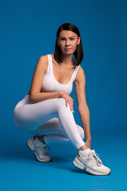 Woman sitting on hunkers after workout on blue surface