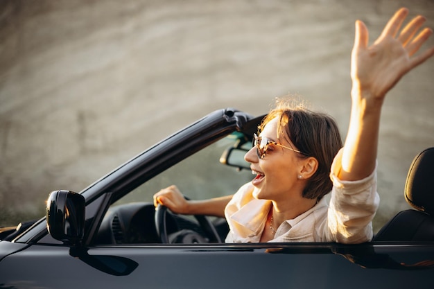 写真 車のカブリオレに座って手を振っている女性