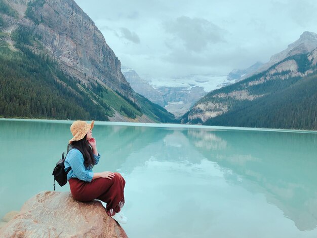 Photo woman sitting at lakeshore against mountains