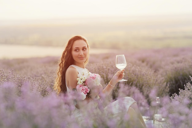 Woman sitting in a lavender field with a glass of wine