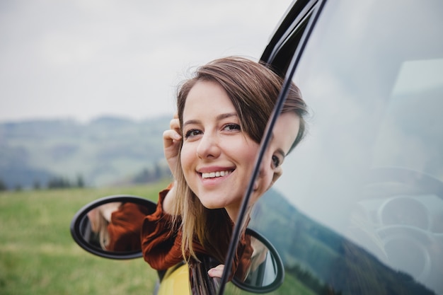 Woman sitting in a little car on a driver place. Located in a mountains.