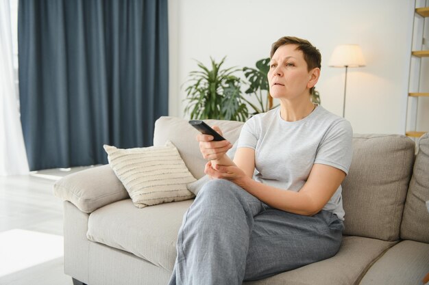 Woman sitting in living room holding remote control smiling