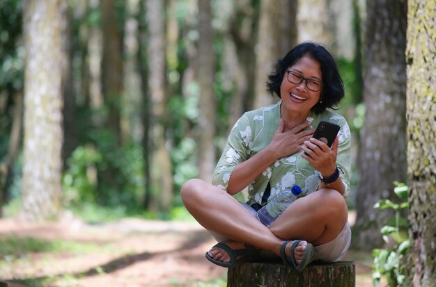 Woman sitting on a log in the park looking happy making a phone call using her smartphone