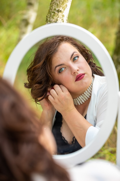 Woman sitting and looking in the mirror in the forest