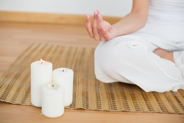 Woman sitting in lotus pose beside white candles