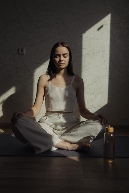 蓮のポーズで座って、自宅でのヨガのトレーニング中に目を閉じて瞑想する女性
