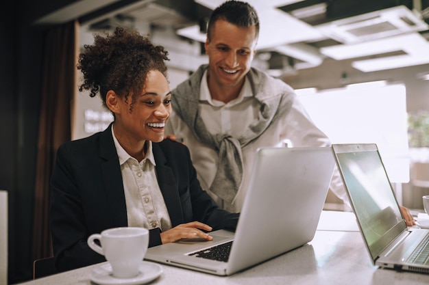 Photo woman sitting man standing joyfully looking at laptop