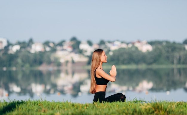 Woman sitting in meditation pose outdoor with gesture namaste from her hands. Side view 