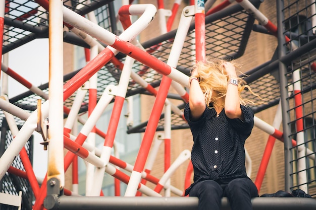 Woman sitting on metal structure against building