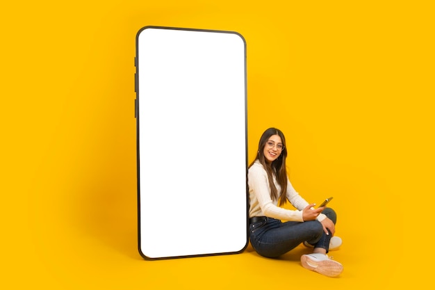 Woman sitting near big huge blank screen mobile phone Smartphone mockup template copy space