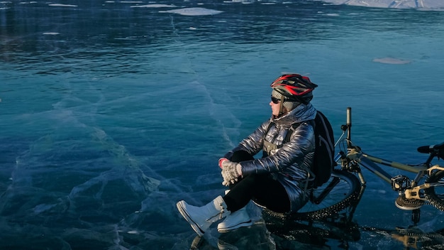 写真 氷の上で自転車の近くに座っている女性女の子のサイクリストは立ち止まりました