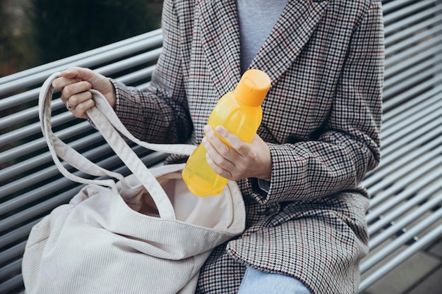 写真 手に黄色いプラスチックの水のボトルを握る屋外のベンチに座っている女性