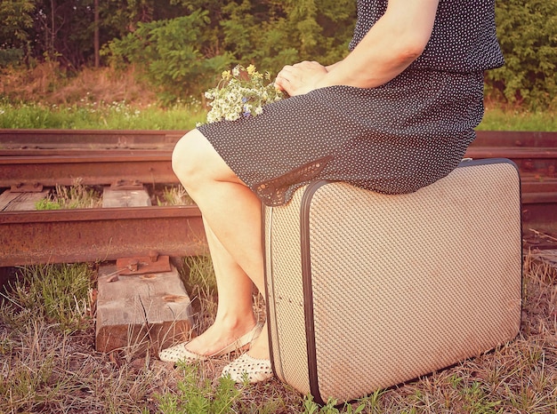 写真 鉄道線路の近くのスーツケースに座っている女性