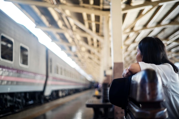 写真 電車のプラットフォームに到着した列車で友人を探すベンチに座っている女性