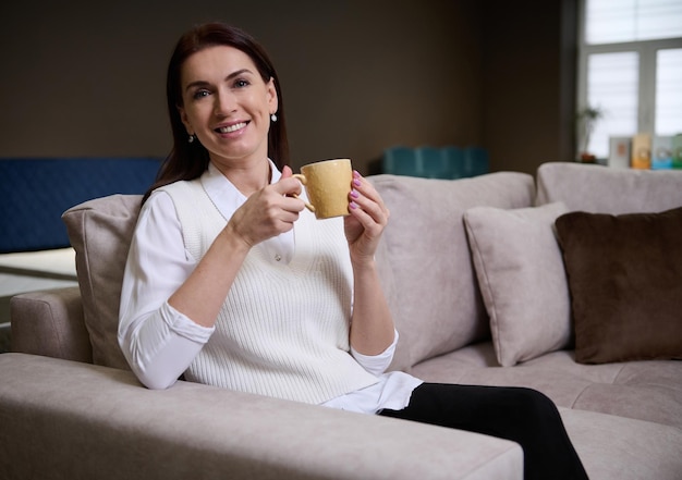 Woman sitting ons sofa enjoying a cup of coffee while picking comfortable sofa in furniture store