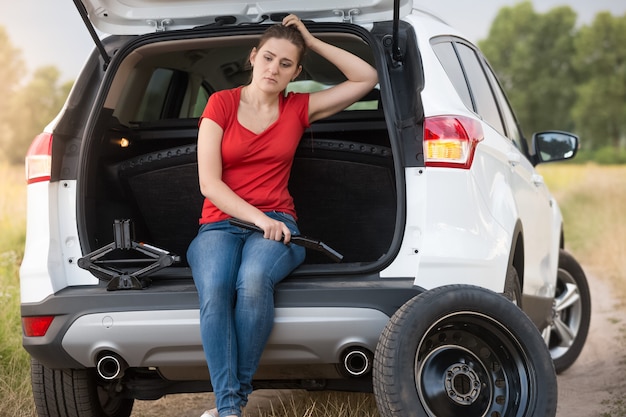 Woman sitting in open trunk of broken car on the countryside road