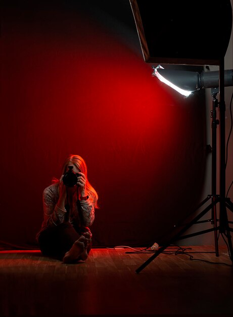 Woman sitting in a photo studio with a camera against a red light background