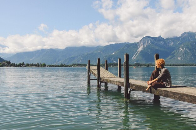 Woman sitting on pier over lake against sky