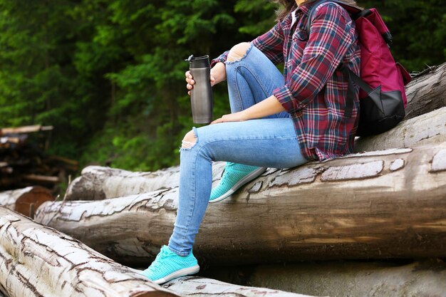 Woman sitting on pile of round logs near the forest