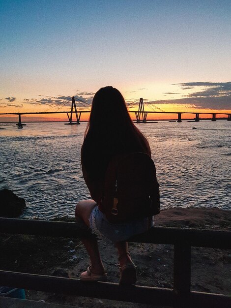 Foto donna seduta su una ringhiera sulla spiaggia contro il cielo durante il tramonto