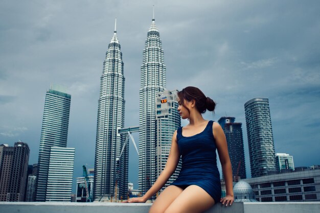 Photo woman sitting on retaining wall against petronas towers