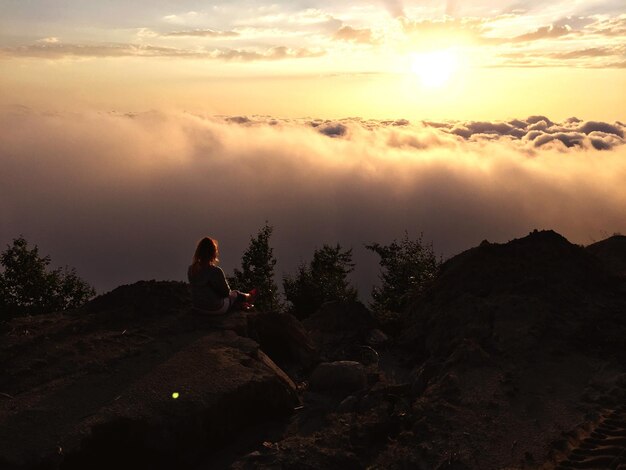 Foto donna seduta su una roccia contro il cielo durante il tramonto