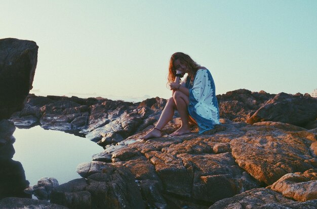 Woman sitting on rock against sky