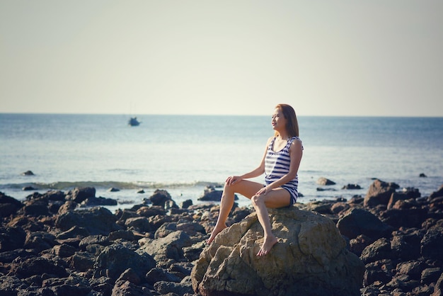 Foto donna seduta su una roccia sulla spiaggia contro un cielo limpido