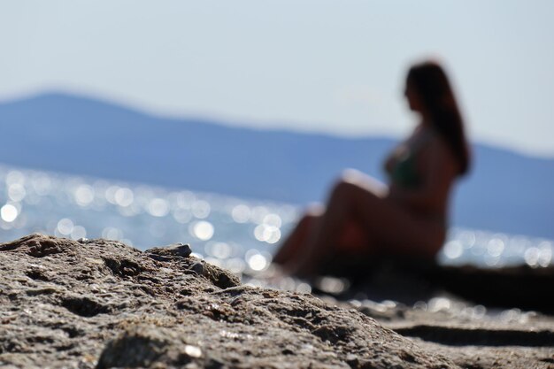 Woman sitting on rock at beach against sky