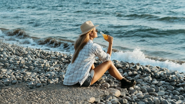 海を見ているジュースと岩の上に座っている女性