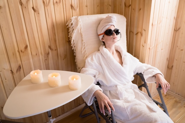 디지털 컬러 테라피 안경을 쓰고 휴식을 취하기 위해 방에 앉아 있는 여성