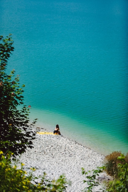 Woman sitting at sand beach looking at blue azure water