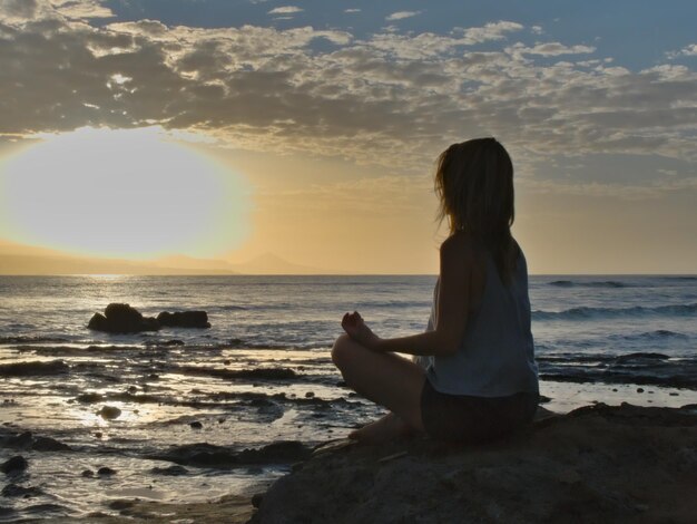 Photo woman sitting on shore at beach against sky during sunset