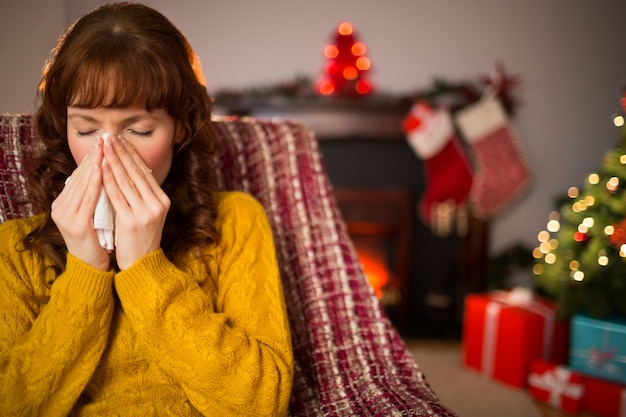 Woman sitting on sofa and blowing her nose at christmas