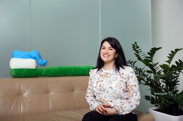 Woman sitting on sofa in clinic reception smiling against big toothbrush