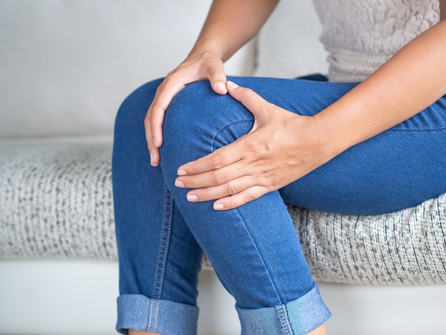 Woman sitting on sofa and feeling knee pain