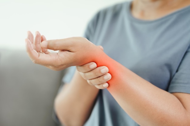 Woman sitting on sofa holds her wrist hand injury with red\
highlight feeling pain