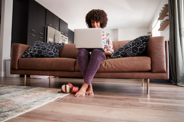 Woman Sitting On Sofa At Home Using Laptop