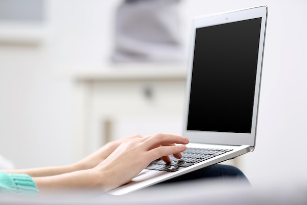 Woman sitting on sofa with a laptop on her knees in a room