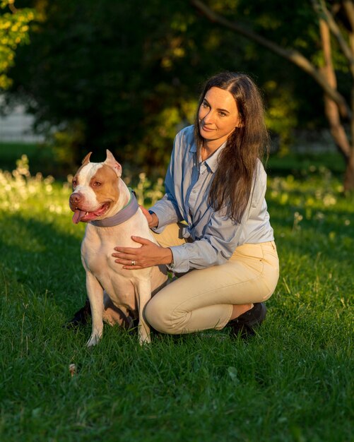 Donna seduta accovacciata e accarezzare con felice american pitbull terrier all'alba