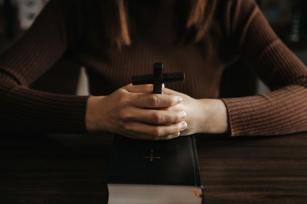 Женщина сидит и изучает Священные ПисанияДеревянный крест в руках Христианские концепции образования Священное Писание открывается и молится БогуxA