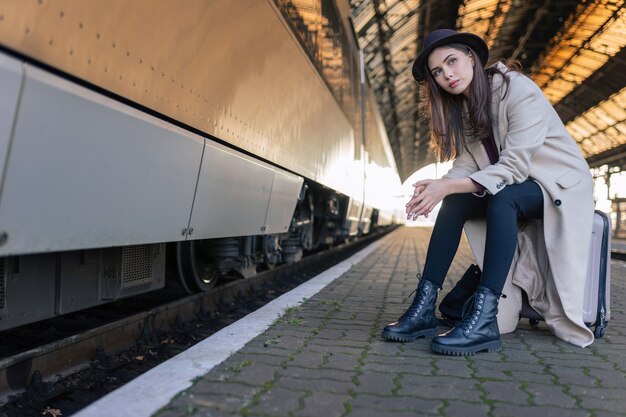 電車を待っているスーツケースに座っている女性