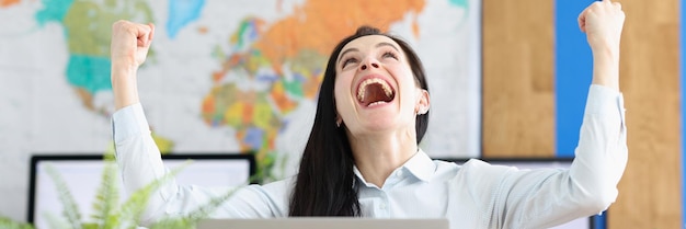 Woman sitting at table in front of computer happy to finish\
business task to pass test successfully