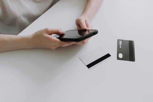 Woman sitting at table holding credit card and using smartphone in hands Online shopping